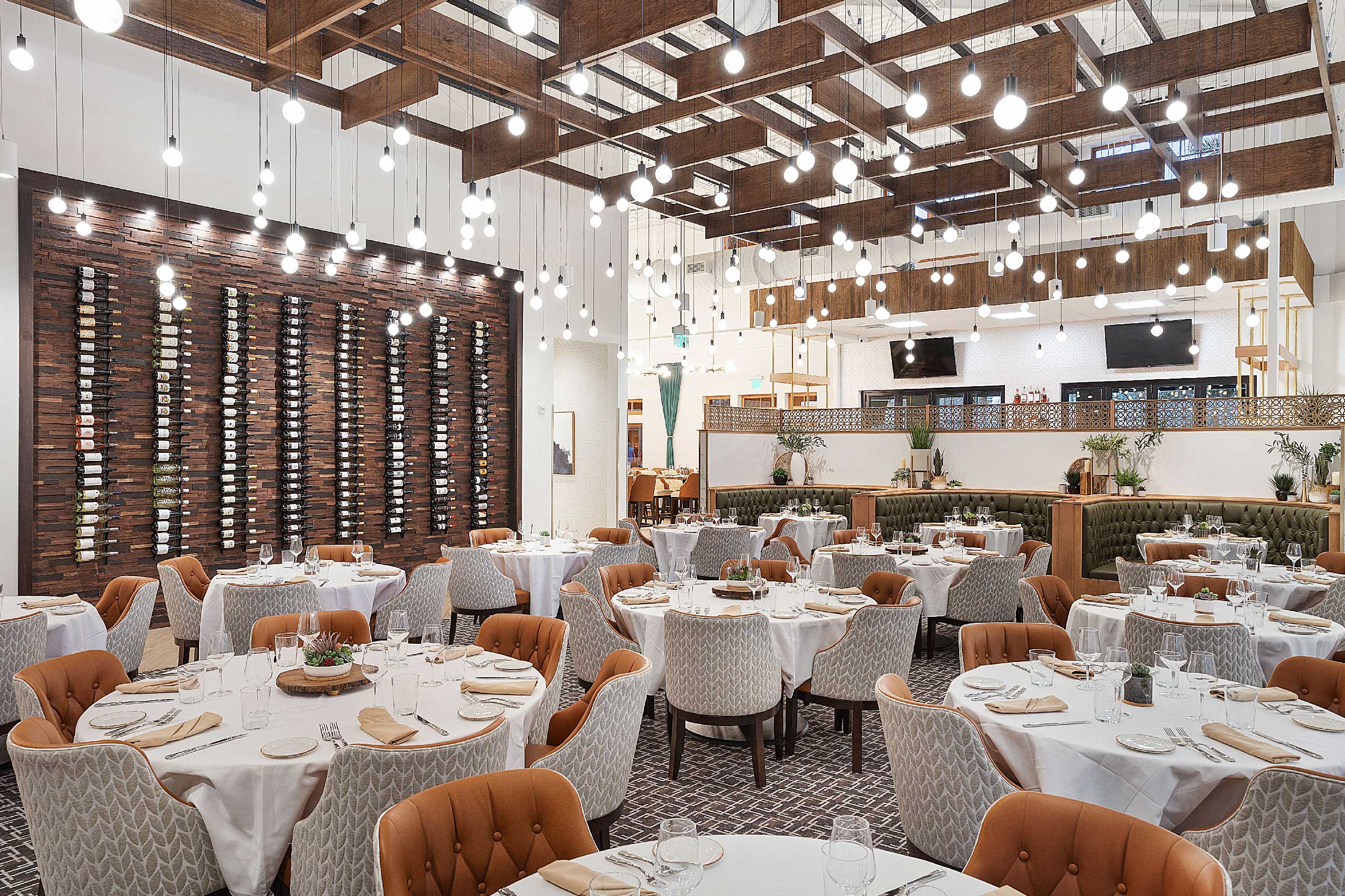 Harvest Restaurant interior main dining area with tables set with chairs and wine bottle wall, hanging light fixtures